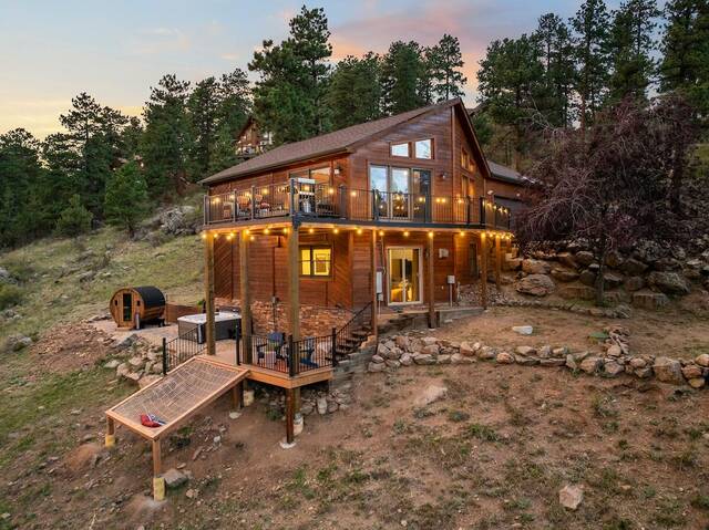 The cabin at twilight, string lights along both decks and the hot tub and barrel sauna lit on the lower pad