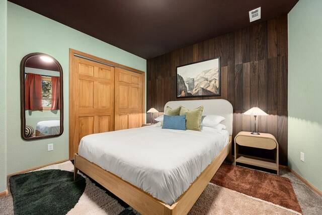 A bedroom with green walls, wood panelling and a queen bed